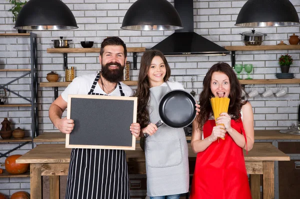 Father, mother and child cooking. Mother father with little girl. Family day. Happy family in kitchen. Little girl with parents in apron. Bearded man with board, copy space. Cooking with passion