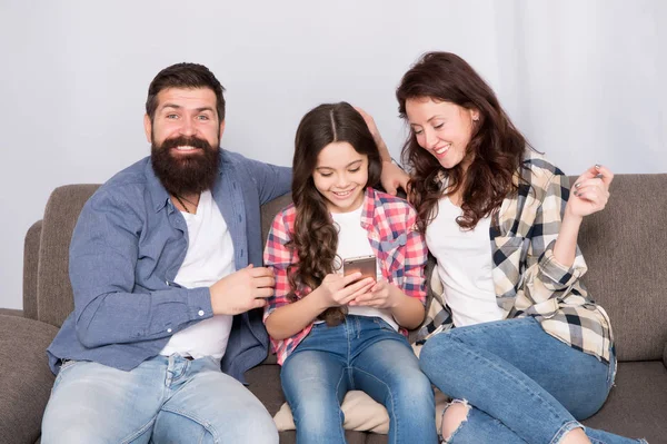 Parental advisory. Family spend weekend together. Child little girl use smartphone with parents. Friendly family having fun together. Mom dad and busy daughter relaxing on couch. Family leisure