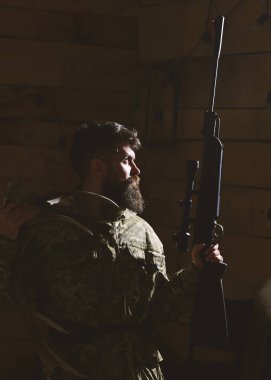 Avcı kavramı. Avcı silahı ve karanlıkta ışıklı geyik boynuzları ile acımasız. Sakallı kamuflaj elbiseler, koyu arka plan giyer. Maço gamekeepers evinde avlamaya hazır sıkı yüzünde