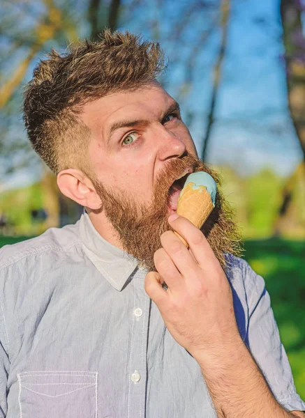 Conceito arrepiante. Homem com longa barba refrigerando com cone de sorvete no dia quente ensolarado, de perto. Homem com barba e bigode no rosto estrito grimace come sorvete, fundo da natureza, desfocado — Fotografia de Stock