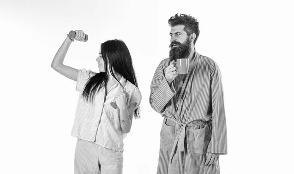 Couple amoureux en pyjama, peignoir isolé sur fond blanc. Fille avec haltère, homme avec tasse de café. Couple, famille au visage endormi, pleine d'énergie. Concept de mode de vie alternatif — Photo