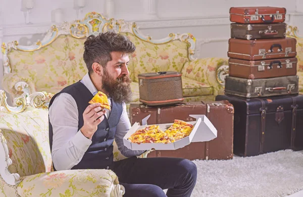 Bon appetit koncepcja. Człowiek z broda i wąsy posiada pole z smaczne, świeże, gorąca pizza. Macho w klasyczne ubrania głodny, trzyma kawałek sera pizzy, zjada, ciesząc się smakiem, tło wnetrze — Zdjęcie stockowe