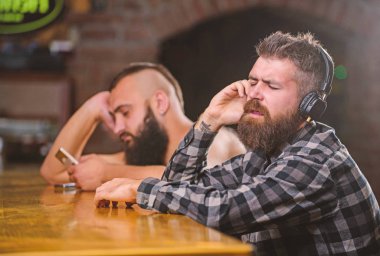 Sayaç bar içecekler sipariş. Erkekler kulaklık ve smartphone bar, rahatlatıcı. İletişim kaçının. Gerçeklik kaçış. Cuma gevşeme çubuk. Hipster sakallı adam harcamak boş olarak bar counter