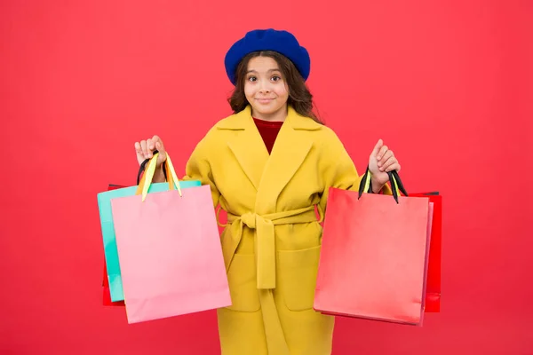 Спостерігали за покупками. Дівчинка мила дитина тримає сумки на червоному тлі. Отримати знижку на покупки на день народження. Модниця обожнює покупки. Задоволення клієнтів. Прем'єрний час купити весняний одяг — стокове фото