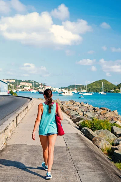 Sexy woman walk along sea in st.thomas, british virgin island. Woman in top and shorts on sea side promenade on sunny day, back view, beach fashion. Summer vacation on island, wanderlust — Stock Photo, Image