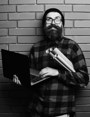 Kaba sakallı, beyaz tenli hippi elinde dizüstü bilgisayar ve el işi kâğıdı tutuyor.