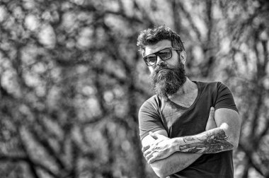 Ciddi sakallı adam kollarını ile ayakta geçti. Yakışıklı adam açık havada poz trendy güneş gözlüğü takıyor dövme ile