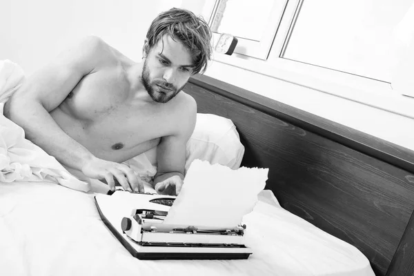 Man writer lay on bed white bedclothes working on new book. Writer author used to old fashioned machine instead of digital gadget. Guy create new chapter use typewriter. Morning inspiration concept