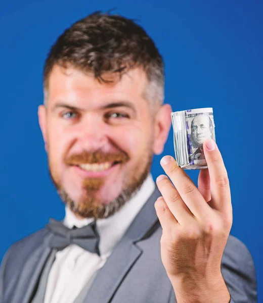 Hipster offer money blue background close up. Easy money concept. Rich businessman hold rolled money. Man bearded hipster hold rolled dollars banknotes. Guy formal suit offer bribe or purchase
