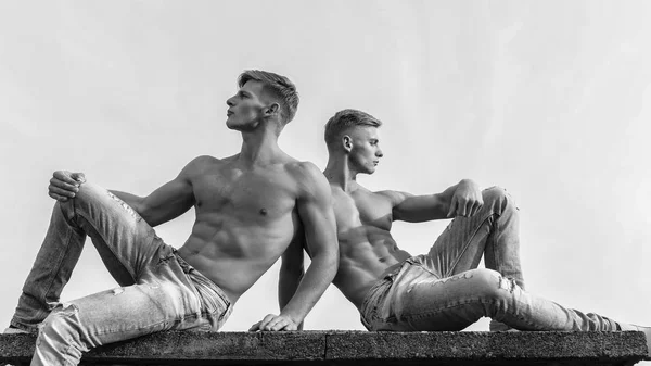 Corps sexy torse attrayant. Le pantalon denim met l'accent sur la masculinité sexualité. Hommes jumeaux frères gars musclés assis relaxer fond de ciel. Hommes musclé musclé musclé bodybuilder détente. Jumeaux attractifs — Photo