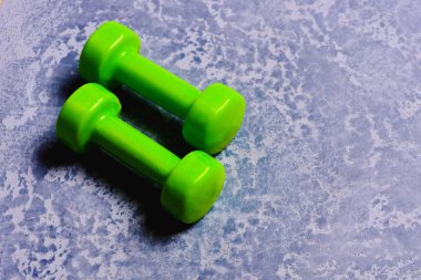 Gri dokuda parlak yeşil plastikten yapılmış dambıllar.