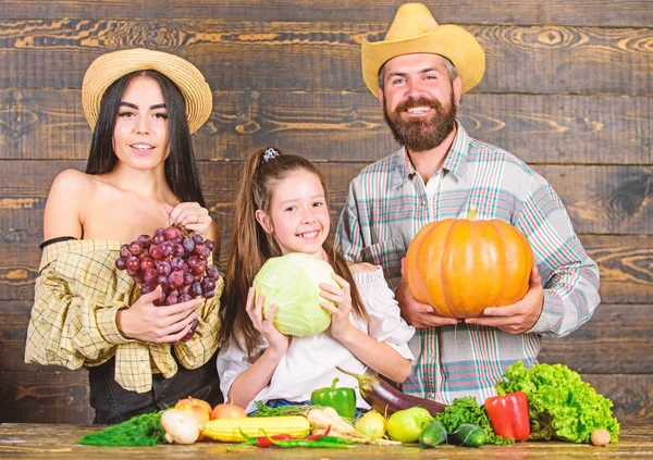 Family rustic style farmers at market with vegetables fruits and greenery. Parents and daughter celebrate autumn harvest festival. Family farm concept. Family farmers with harvest wooden background