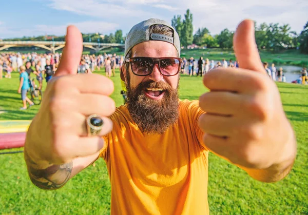 Highly recommend top list events. Hipster visiting event picnic fest or festival. Man cheerful face shows thumb up. Man bearded in front of crowd riverside background. Book ticket now summer festival