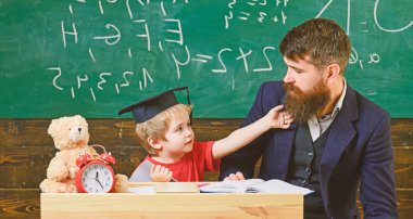 Öğretmen ve öğrenci kolej, kara tahta arka plan içinde. Neşeli okurken, dikkat eksikliği dikkat dağıtan çocuk. Yaramaz çocuk kavramı. Evlat, küçük çocuk öğretmen öğretir sakal, baba