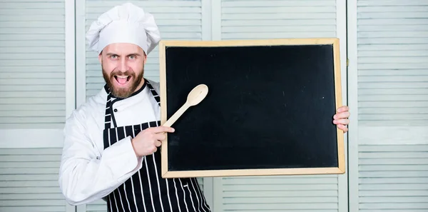 Enseñando a los estudiantes a cocinar. Jefe de cocina enseñando clase magistral en la escuela de cocina. Maestro cocinero dando clases de cocina. Educación culinaria. Hombre apuntando cuchara de madera en pizarra vacía, espacio para copiar —  Fotos de Stock