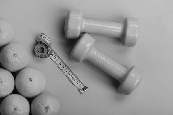 Oranges near dumbbells, cyan measuring tape on green background, — Stock Photo, Image