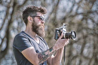 Fotoğrafçı sakal ve bıyık amatör fotoğrafçı doğa arka plan ile. Fotoğraf çekimi ile meşgul uzun sakallı adam. Fotoğrafçı kavramı. Adam sakallı hippi fotoğrafçı tutun vintage fotoğraf makinesi.