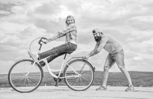 Mujer paseos bicicleta cielo fondo. El hombre ayuda a mantener el equilibrio y andar en bicicleta. Cómo aprender a andar en bicicleta como adulto. Chica en bicicleta, mientras que el novio la apoya. Técnica de ciclismo. Aprende ciclismo con apoyo — Foto de Stock