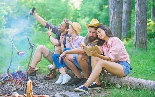 Turistas sentar log perto de fogueira tirar foto no smartphone. Amigos no momento da captura de férias. Amigos perto de fogueira desfrutar de férias e comida assada. Homem tirando foto perto de fogueira natureza fundo — Fotografia de Stock