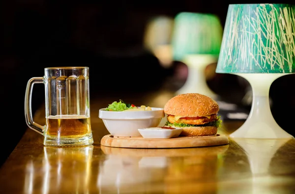 Snack alto en calorías. Hamburguesa y papas fritas y salsa de tomate sobre tabla de madera. Deliciosa hamburguesa. Hamburguesa con carne de queso y ensalada. Comida de bar y jarra de cerveza. Concepto de comida rápida. Menú hamburguesa —  Fotos de Stock