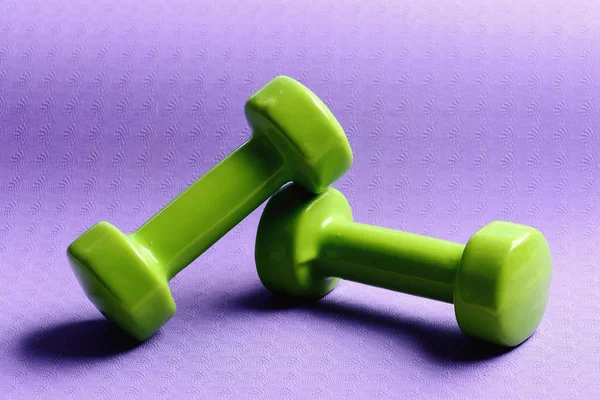 Dumbbells made of green plastic on purple background