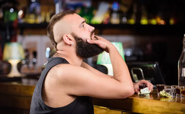 Man drunk sit alone in pub. Alcoholism and depression. Alcohol addicted concept. Hipster brutal man drinking alcohol ordering more drinks at bar counter. Guy spend leisure in bar with alcohol