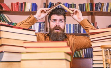 Son Tarih kavramı. Adam Kitaplığı'nda, eğitim sırasında kitaplar, kitap rafı arka plan üzerinde yığınları arasında şok yüzünde. Öğretmen veya sakallı öğrenci kitabı, defocused çatı yapım masada oturur