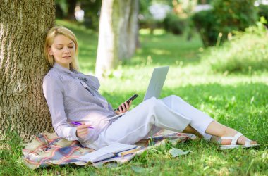Eğitim teknolojisi ve internet kavramı. Dizüstü bilgisayar işleriyle açık havada ağaç gövdesinde yağsız olan kadın. Park içinde laptop ile kız iş çimenlerin üzerinde oturmak. Doğal çevre ofisi. İş açık havada faydaları