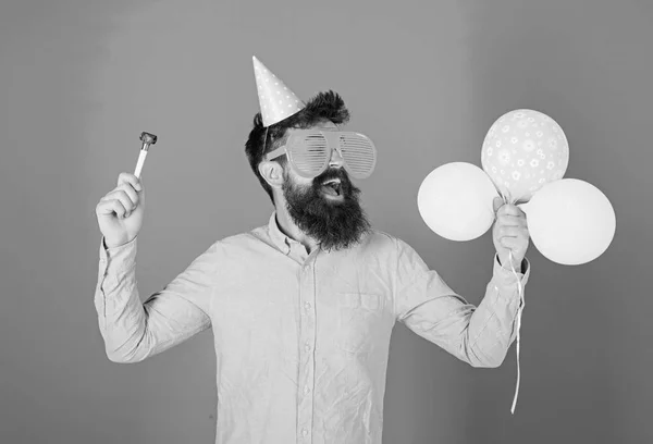 Homem com barba e bigode na cara feliz segura balões de ar, fundo azul. Conceito de festa. O tipo de chapéu de festa com atributos de férias celebra. Hipster em óculos gigantes celebrando aniversário — Fotografia de Stock