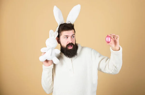 A Páscoa está a chegar. Hipster com longas orelhas de coelho segurando a lebre poedeira. Homem barbudo com brinquedo de coelho e ovo de Páscoa. Celebração de férias de primavera. Coelho da Páscoa entregando ovos coloridos — Fotografia de Stock