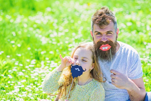 Pai posando com lábios e criança posando com barba foto cabine atributo. Conceito de papéis de gênero. O pai e a filha sentam-se no relvado, a relva no fundo. Família passar o lazer ao ar livre — Fotografia de Stock