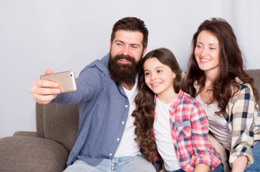 Aile birlikte hafta sonu geçirmek. Smartphone için selfie kullanın. Dostu aile birlikte eğleniyor. Anne baba ve kızı kanepede rahatlatıcı. Aile fotoğrafı için poz. Mutlu anları yakalayın. Aile selfie