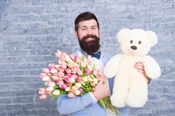 Dia Internacional da Mulher. Homem usar azul smoking arco gravata segurar flores buquê. A surpresa vai derreter-lhe o coração. Homem romântico com flores e ursinho. Um presente romântico. Macho se preparando encontro romântico — Fotografia de Stock