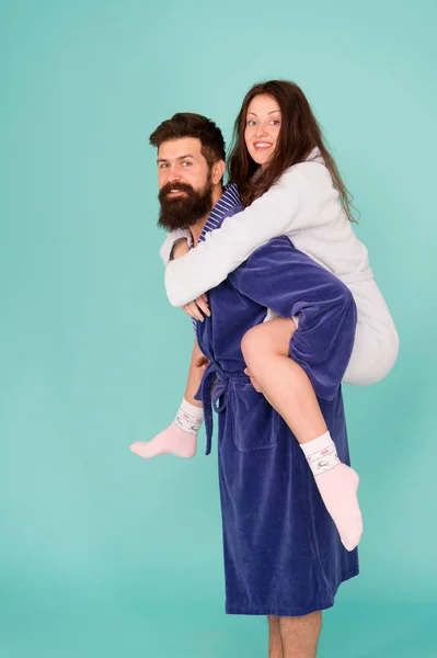 Handsome young man piggybacking beautiful woman. Couple in bathrobes having fun turquoise background. Lets stay at home and have fun. They always have fun together. Enjoying every second together