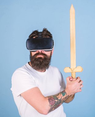 Oyun kavramı. Hipster ciddi bir yüz üzerinde sanal gerçeklik oyun oyun keyfini çıkarın. Adam kafa monte ekran ile kılıç tutan, dövüş Vr gözlük, açık mavi renkli sakallı Vr. adam oyunu oyna