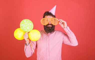 Hippi dev güneş gözlüğü Doğum günü kutluyor. Sakal ve bıyık mutlu yüz tutan grup hava balonları, kırmızı arka plan üzerinde olan adam. Kutlama kavramı. Parti şapkalı adamı tatil kutluyor