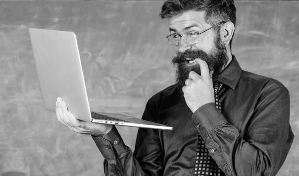 Hipster-Lehrer mit Brille und Krawatte hält Laptop beim Internetsurfen. Lehrer bärtigen gerissenen Mann modernen Laptop surfen Internet-Kreidetafel Hintergrund. Interessante Informationen. Rettungsring für die Schule — Stockfoto