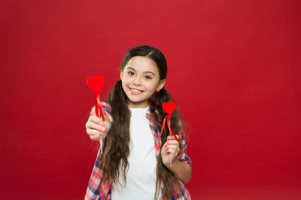 This is a day to say I love you. Small girl giving hearts on sticks. Cute girl with small red hearts. Small child with heart shaped decorations. Happy valentines day. The holiday of love and romance