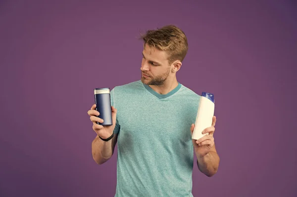 Macho mantenga botellas de champú y gel sobre fondo violeta. Hombre de camiseta azul con tubos sobre fondo púrpura. Cuidado de la piel y el cabello. Salud y salud. Cosmético para spa y bañera o ducha . — Foto de Stock