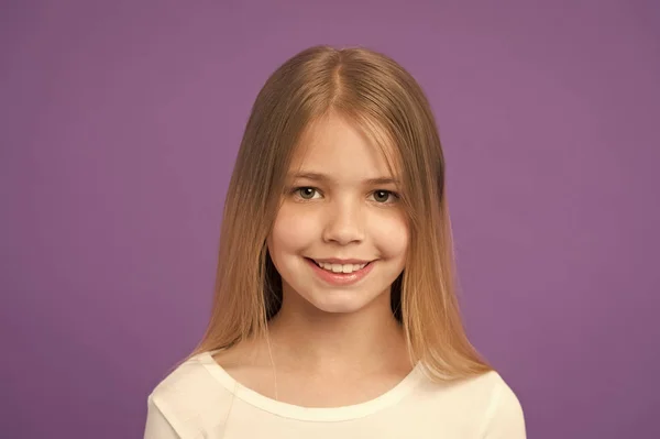 Look beauté et soin de la peau. Petite fille sourire sur fond violet. Enfant avec une peau fraîche sur le visage mignon. Enfant de beauté avec un look heureux et de longs cheveux blonds sur fond violet. Garde d'enfants et d'enfants — Photo