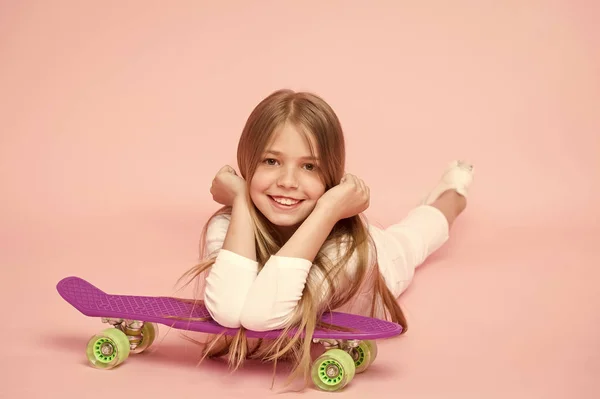 ピンクの背景にスケート ボードと小さな女の子の笑顔。ロングボードを浮かべて子供スケーター。階スケート ボード子供嘘。小児期のライフ スタイルとアクティブなゲーム。スポーツ活動とエネルギー、パンチの効いたパステル — ストック写真