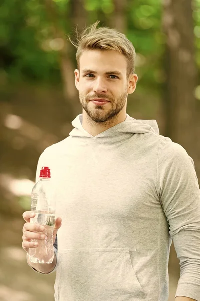 Bebe algo de agua. Hombre guapo corredor sostiene botella de agua todo el entrenamiento en el parque. Hombre atleta ropa deportiva refrescante. Concepto de deporte y estilo de vida saludable. Atleta beber agua después de entrenar en el parque — Foto de Stock