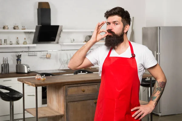 Як перетворити кулінарію в звичку. Чоловік бородатий гіпсовий червоний фартух стоїть на кухні. Кухонний магазин меблів. Готуємо на новій кухні. Вихідні починаються зі смачного сніданку. Потрібно кулінарне натхнення — стокове фото
