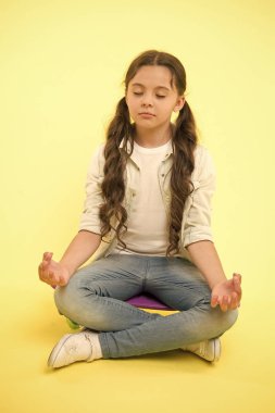 Küçük kız, sarı arka planda panoda oturmuş meditasyon yapıyor. Yoga zamanı. Hippi çocuk aktivitesi. Konsantrasyon ve meditasyon. Sakinleşiyorum. Paten kaymak onun hayatı. Rahatlama egzersizi.