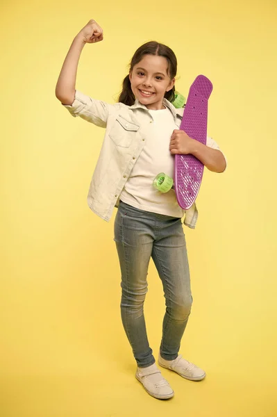 乗ることができる。子供の女の子幸せなペニーボードを保持します。女の子幸せな顔はペニーボード黄色の背景を運ぶ。子供はペニーボードに乗ることを学んだ。子供はプラスチックスケートボードが好きパワージェスチャーを示しています。女の子の力 — ストック写真