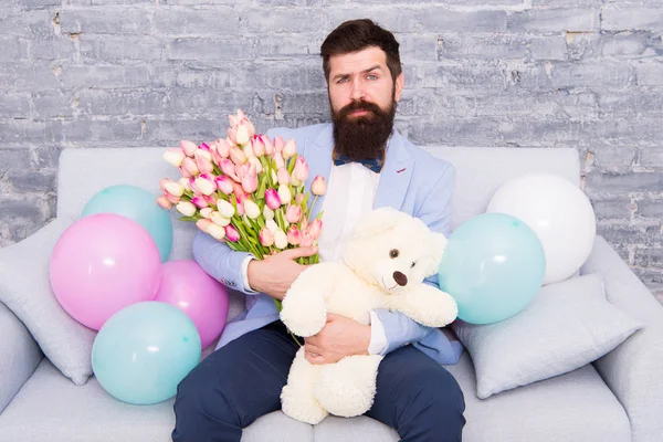 Best boyfriend ever. Romantic man with flowers and teddy bear sit on couch waiting girlfriend. Romantic gift. Macho getting ready romantic date. Man wear blue tuxedo bow tie hold flowers bouquet