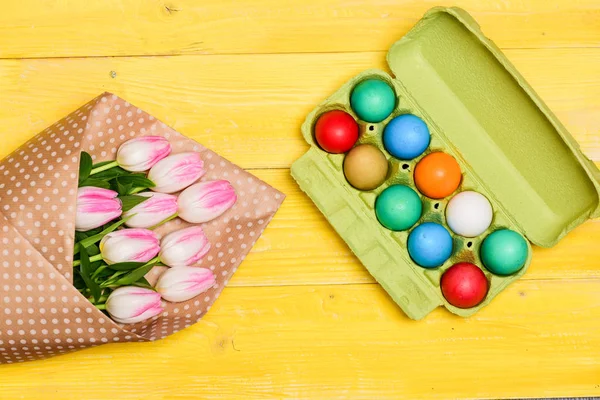 Paskalya yumurtası toplama. Renkli yumurta ve buket taze Lale çiçek sarı arka plan üzerinde görünümü top. Gelenek Paskalya kutlamak. Samimi selamlar. Paskalya vibes. Bahar tatili. Mutlu Paskalya sezon — Stok fotoğraf