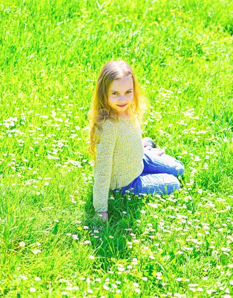 Fille s'assoit sur l'herbe à la prairie, fond vert. L'enfant profite du soleil printanier lorsqu'il est assis à la prairie. Concept Heyday. Fille sur le visage souriant passer ses loisirs à l'extérieur — Photo