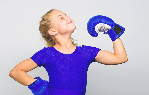 Воспитание лидерства и победителя. Феминистское движение. Сильный ребенок гордый победитель соревнования по боксу. Девочка счастливая победительница в боксёрских перчатках позирует на сером фоне. Она чувствует себя победительницей
