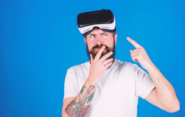 Sakal ve bıyık Vr gözlük, mavi arka plan ile olan adam. Adam Vr gözlük veya baş ile ekran monte. Gadget'ı işaret parmağı ile işaret düşünceli yüzündeki hippi. VR teknolojisi kavramı